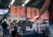 Inside CDC’s Urgent Ebola Volunteer Plea A traveler holding a suitcase in an airport terminal with a flight information display in the background