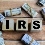 IRS REFUNDS – Billions Up for Grabs! Wooden blocks spelling IRS surrounded by rolled currency notes