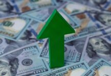 Green arrow pointing upwards on a background of hundred dollar bills