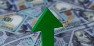 Green arrow pointing upwards on a background of hundred dollar bills
