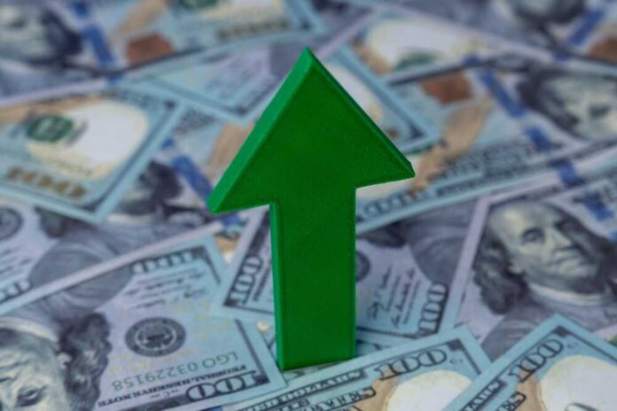 shutterstock_2645459483.jpg Green arrow pointing upwards on a background of hundred dollar bills