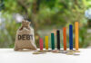 Debt Bomb Forces Painful Cuts Debt sack with rising financial graph bars.