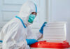 Healthcare worker in protective gear disposing of waste