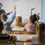 Culture War Hits Classrooms — Texas Goes Biblical Students raising hands in a classroom with a teacher.