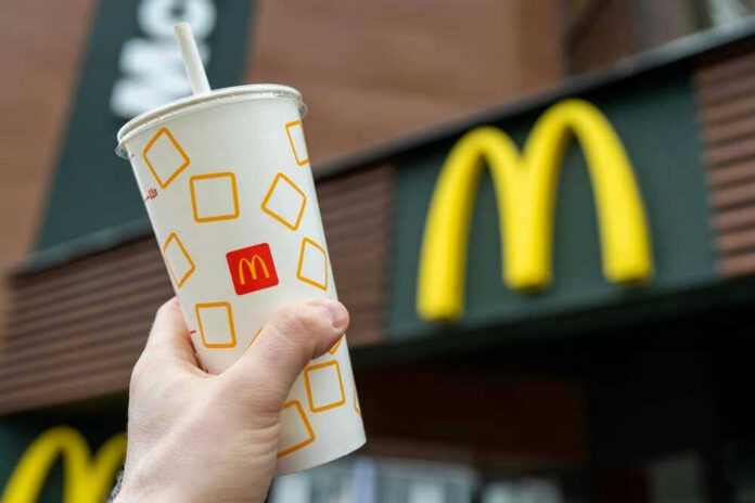 shutterstock_2161712859 Hand holding McDonalds cup in front of restaurant sign.