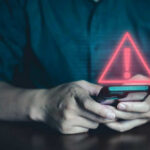 Person holding phone with warning symbol displayed.