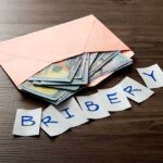 Envelope with cash and notes spelling bribery on wooden table