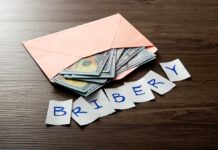 Envelope with cash and notes spelling bribery on wooden table