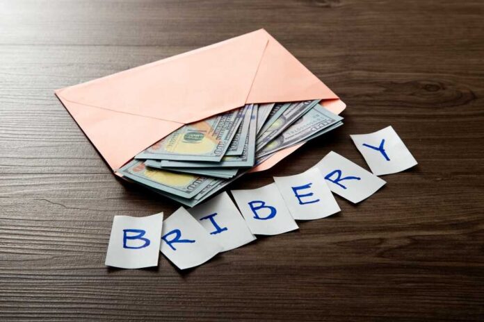 Envelope with cash and notes spelling bribery on wooden table
