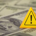 Hidden War Tax Draining Family Budgets A yellow warning sign placed on a background of dollar bills