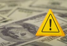 Hidden War Tax Draining Family Budgets A yellow warning sign placed on a background of dollar bills