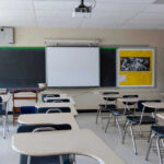 New School Hall Monitor: Drones? Empty classroom with desks, projector, and chalkboard.