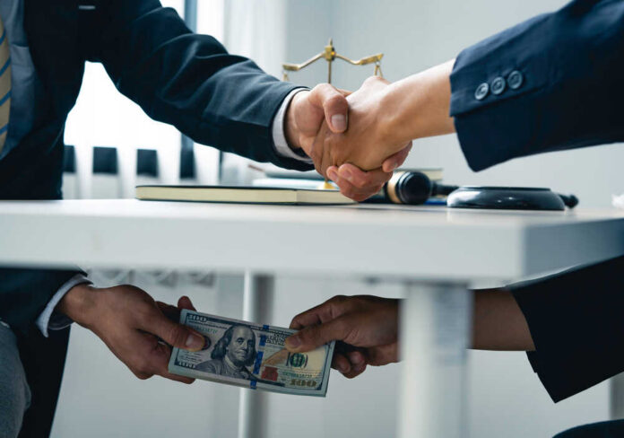 Business,People,Shaking,Hands,And,Give,An,Under-the-table,Bribe,To Businessmen handshake while cash is passed under the table