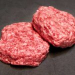 Beef Drops Big — Politics Erupt Two raw ground meat patties on a dark surface