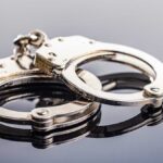 Famed Quarterback Cuffed, Arrested Close-up of metallic handcuffs on a reflective surface