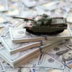 $37.5B? Pentagon’s Iran Math Explodes A toy tank placed on stacks of hundred-dollar bills