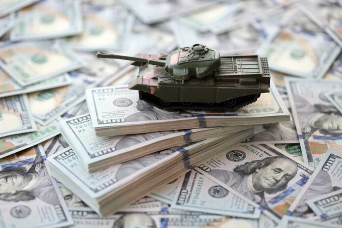 Toy,Tank,On,Us,Hundred,Dollar,Bills,Banknotes,Close,Up. A toy tank placed on stacks of hundred-dollar bills