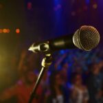 Shock Death Stuns Music World Close-up of a microphone in front of a blurred audience at a concert
