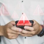 Hands holding a smartphone with warning icons overlay