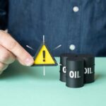 ALERT: Oil Panic Nears $100 After Tanker Blasts A person holding a warning sign next to oil barrels
