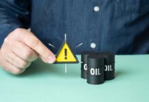 ALERT: Oil Panic Nears $100 After Tanker Blasts A person holding a warning sign next to oil barrels