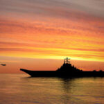 Drought Unmasks WWII Time Bombs Silhouette of an aircraft carrier at sunset.