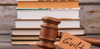 A wooden gavel with a tag reading 'Guilty' next to stacked books
