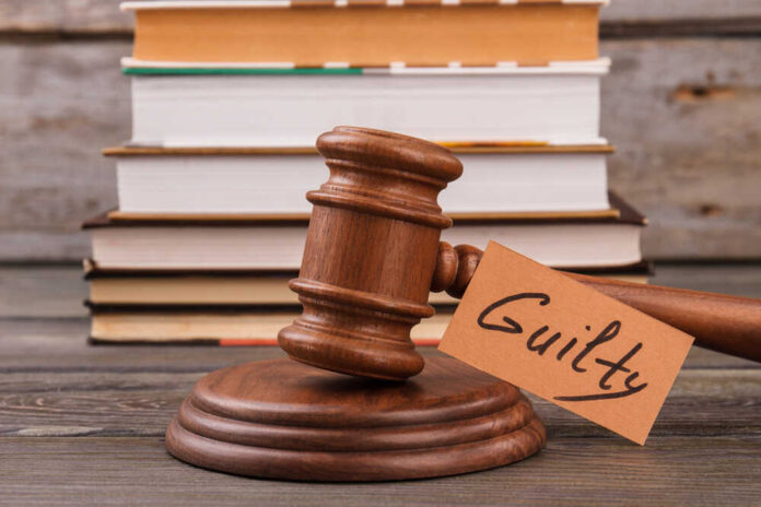 A wooden gavel with a tag reading 'Guilty' next to stacked books