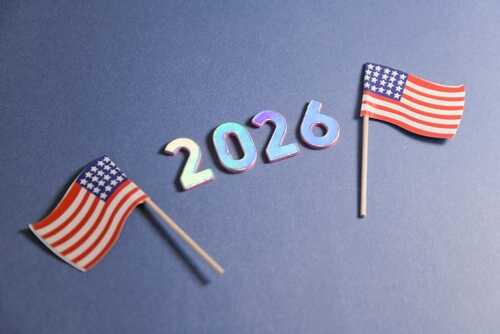 2026,Metallic,Numbers,With,Mini,American,Flags,On,Blue,Background Two small American flags next to the numbers 2026 on a blue background