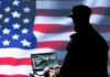 Silhouette of a person using a laptop before a large US flag
