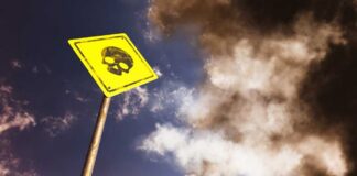 Yellow warning sign with skull symbol under dramatic cloudy sky