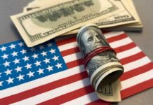 FBI Dangles $25K — Details HERE! A roll of hundred dollar bills placed on an American flag
