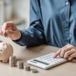 Broke Math Drives Kids Home Person placing a coin into a piggy bank while using a calculator