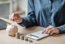 Person placing a coin into a piggy bank while using a calculator