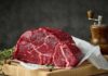 Mystery Beef Pulled — Crucial Details HERE! A raw cut of beef on a wooden board with herbs and a pepper grinder