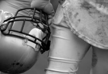 TRAGEDY: NFL’s Grim Math – One In Four Football player holding helmet, dirty uniform close-up.