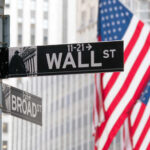 Deli Scam Explodes To $100 Million Wall Street and Broad Street signs with American flags in background