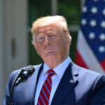 Donald Trump speaking with US flag in the back.