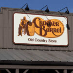 Dinner War Erupts at Cracker Barrel Sign for Cracker Barrel Old Country Store featuring a man sitting on a barrel