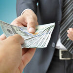 Hidden Millionaires Quietly Take Over A person handing over a stack of cash to another individual in a suit