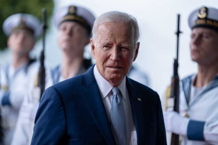 shutterstock_2376139637 Joe Biden stands in front of uniformed honor guards