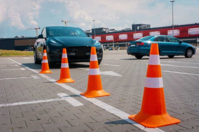 A black electric car parked near orange traffic cones in a parking lot