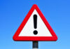 40,000 Mega-Bombs – Why Now? A triangular warning sign with an exclamation mark against a blue sky