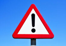 40,000 Mega-Bombs – Why Now? A triangular warning sign with an exclamation mark against a blue sky