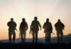 Moon War Warning Shocks U.S. Troops Five armed soldiers silhouetted against sunset background.