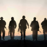 Moon War Warning Shocks U.S. Troops Five armed soldiers silhouetted against sunset background.