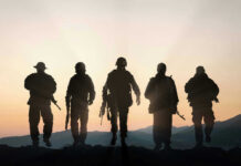 Moon War Warning Shocks U.S. Troops Five armed soldiers silhouetted against sunset background.