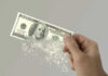 Hand holding a disintegrating hundred dollar bill.