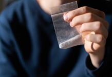 Teen Death Triggers Massive Bust Hand holding a small plastic bag with white powder