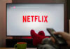 Person watching Netflix with remote and drink.